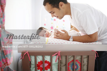 A 2 months old baby girl on a changing table, her dad taking care of her