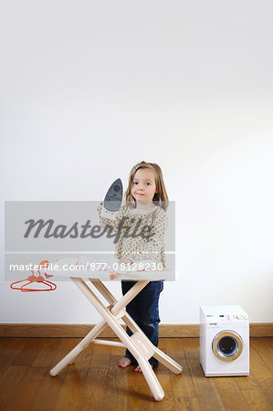 A 3 years old girl playing with an iron and ironing board for child