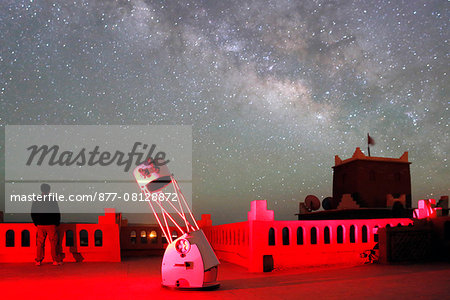 Morocco. Draa Valley. Zagora region. Milky Way and starry sky above a kasbah. Man admiring the sky. Telescope.