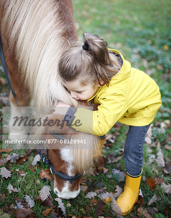 A little girl kissing a pony while he is grazing