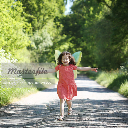 s A 5 years old girl wearing butterfly wings, in the countryside