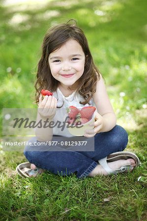 A 5 years old girl eating  strawberries in the countryside