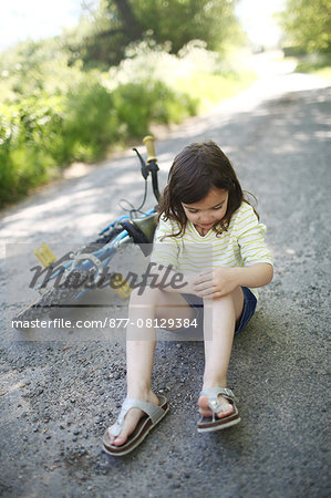 A 5 years old girl near her bike, after falling on a country road