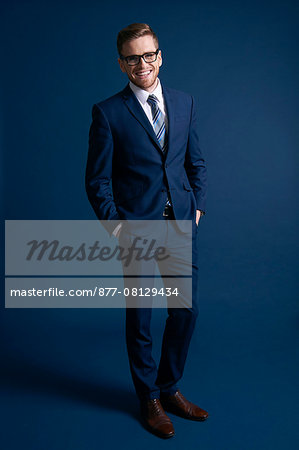 man in blue suit, glasses, blue background, smiling; tie