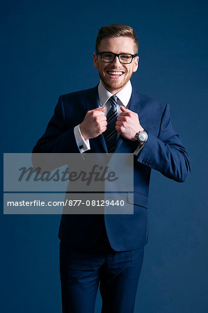 man in blue suit, glasses, tie, blue background, laughing, watch