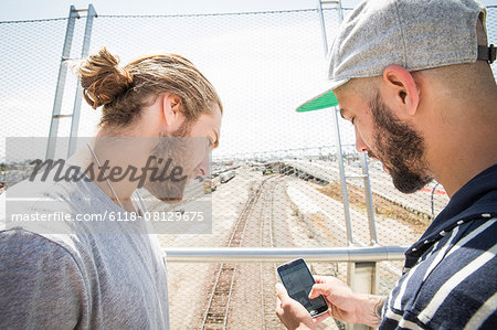 Two young men standing on a bridge, looking at mobile phone.