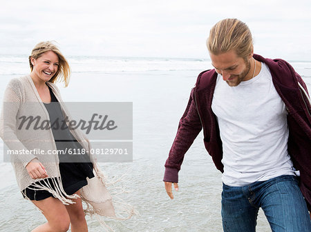 Young man and young woman walking on a beach, smiling.