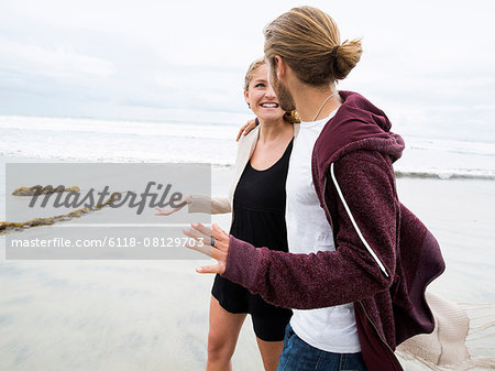 Young man and young woman walking on a beach, smiling.