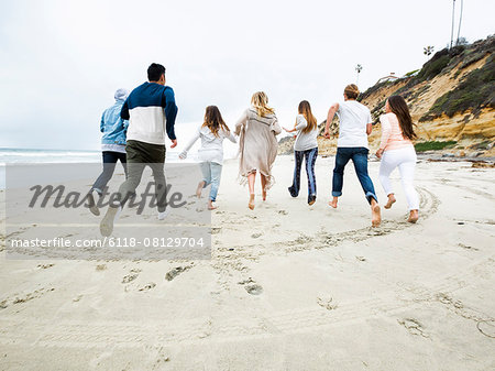 A group of young men and women running on a beach, having fun.