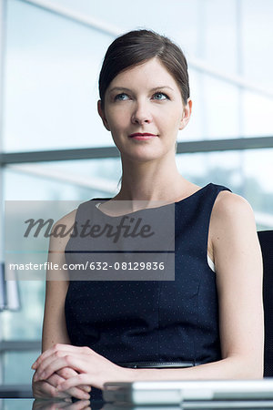 Businesswoman sitting at desk, looking away in thought, portrait