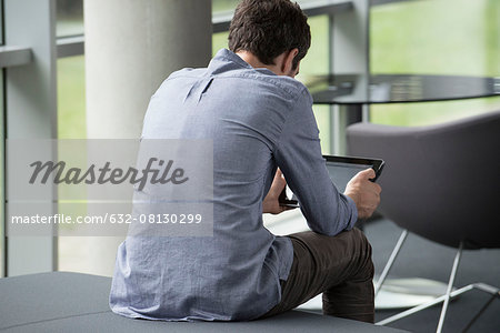 Man sitting alone, looking at digital tablet, rear view