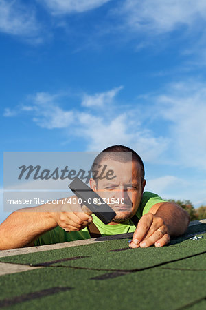 Man fastening bitumen roof shingles with nails and hammer - copy space