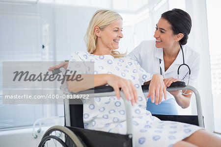 Happy doctor smiling at her patient in wheelchair in hospital