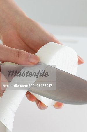 Close up of woman's hands peeling radish with a kitchen knife