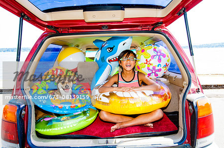 Child poses with his dog in the open trunk of a car full of beach toys and floaties