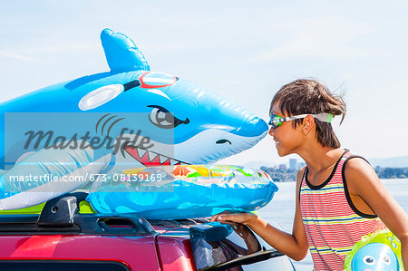 Child poses beach toys and floaties on the roof of a car