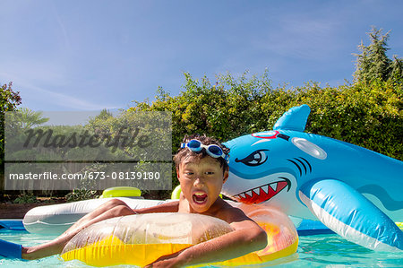 Boy pretends to be attacked by an inflatable shark in a pool