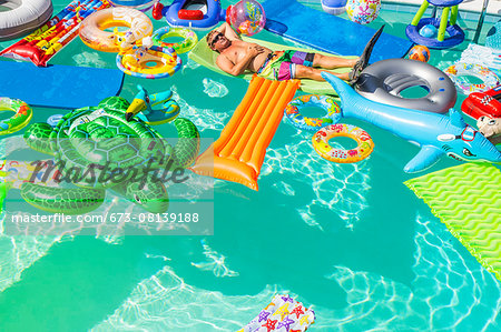 Man wearing flippers floats in a pool full of inflatable toys