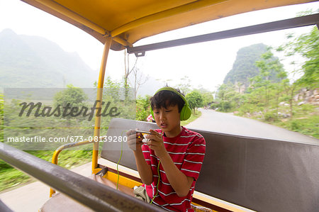 Boy wearing headphones uses an electronic device while riding a village jitney