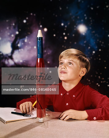 1960s BOY WITH MODEL ROCKET DAYDREAMING LOOKING AT ROCKET ON DESK STAR GALAXY BACKGROUND