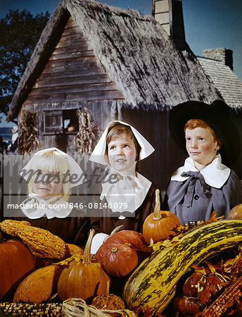 1960s 3 KIDS DRESSED IN PILGRIM COSTUMES CLOTHES FOR THANSKGIVING COMPOSITE WITH PLIMOUTH COLONY BACKGROUND AND PUMPKINS