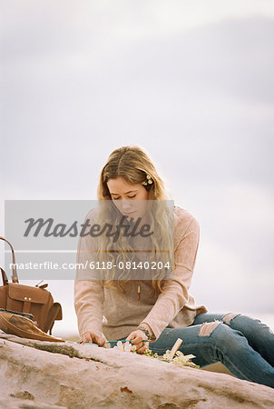 Woman sitting on a rock in a desert, a leather bag standing beside her.