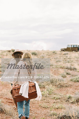 Two women walking towards a 4x4 parked in a desert.