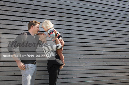 Family by clapboard wall, mother holding son