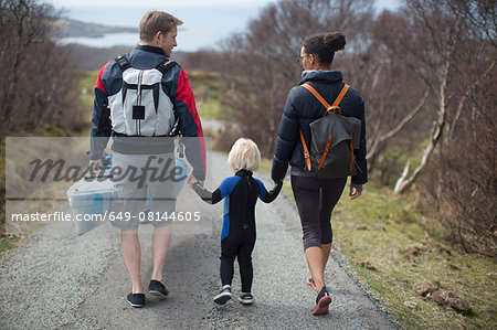 Family walking on country road holding hands, rear view