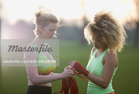 Two women applying hand straps for boxing gloves in the park