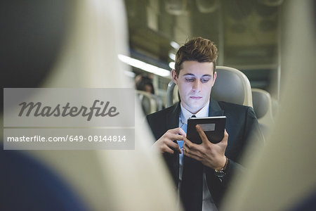 Portrait of young businessman commuter using digital tablet on train.