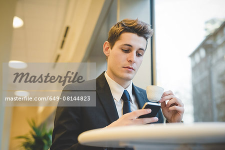 Portrait of young businessman sitting in cafe using digital tablet and mobile phone.