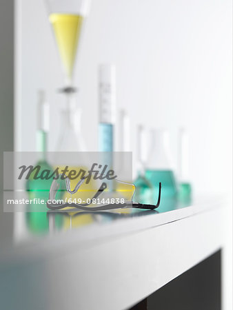 Laboratory safety glasses on lab bench with a chemical experiment in background Laboratory safety glasses on lab bench with a chemical experiment in background