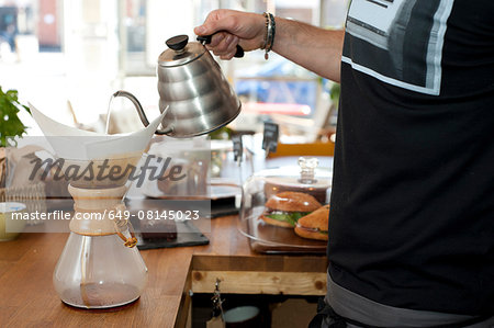 Hand of cafe waiter pouring boiling water into filter coffee pot