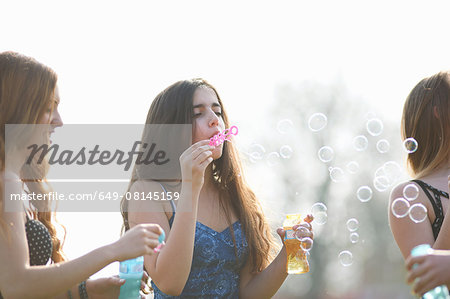 Three teenage girls blowing bubbles in park