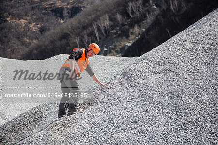 Quarry worker measuring on gravel mound at quarry