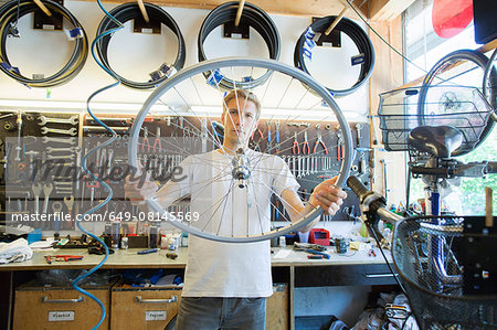 Mid adult man in repair shop looking through bicycle wheel