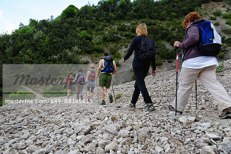 Row of six male and female mature hikers hiking in stoney valley