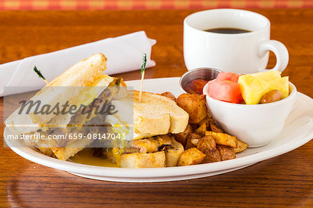 A breakfast sandwich with fried potatoes, fruit salad and coffee