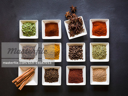 Various spices in square dishes on a chalkboard surface