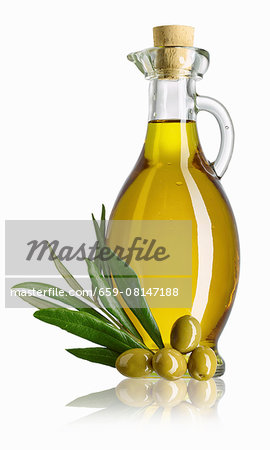 A carafe of olive oil, a sprig of olive leaves and green olives