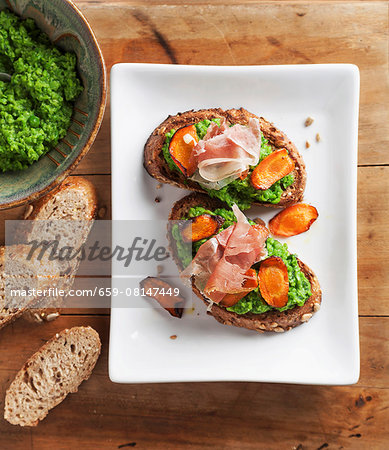 Crostini topped with pea cream, roasted carrot slices and ham