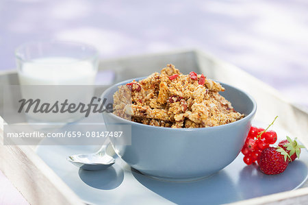 A bowl of muesli on a tray with fruit and a glass of almond milk next to it
