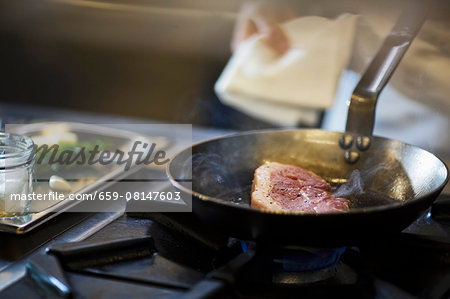 A chef preparing a steak in a commercial kitchen