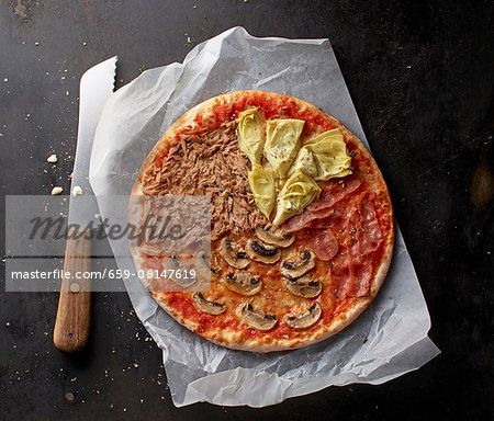 A tuna, mushroom, Parma ham and artichoke pizza on a piece of paper with a knife