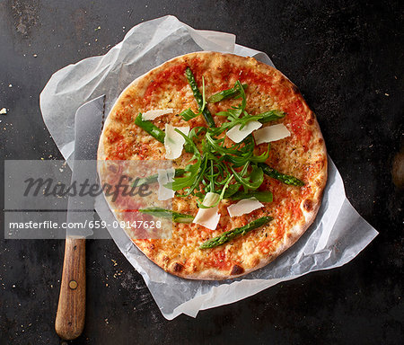 Pizza Margherita with asparagus, rocket and grated Parmesan on a piece of paper with a knife