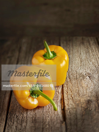 Two yellow peppers on a wooden surface