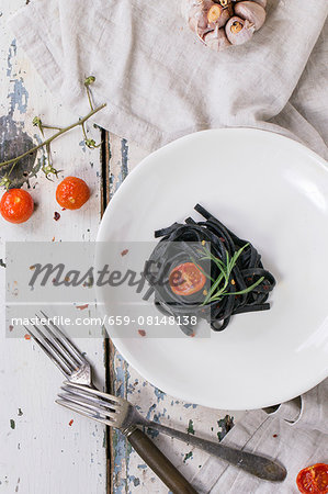 Black tagliolini with baked tomatoes and garlic on old wooden table Black tagliolini with baked tomatoes and garlic on old wooden table