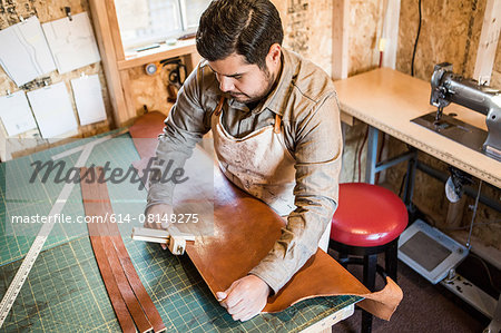 Leather craftsman using wooden clamp on workshop bench