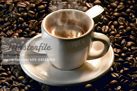 A steaming cup of espresso on roasted coffee beans A steaming cup of espresso on roasted coffee beans